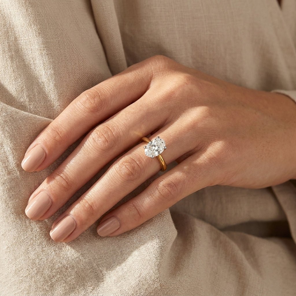 2 carat oval lab grown diamond engagement ring on woman ring finger close-up with beige linen background