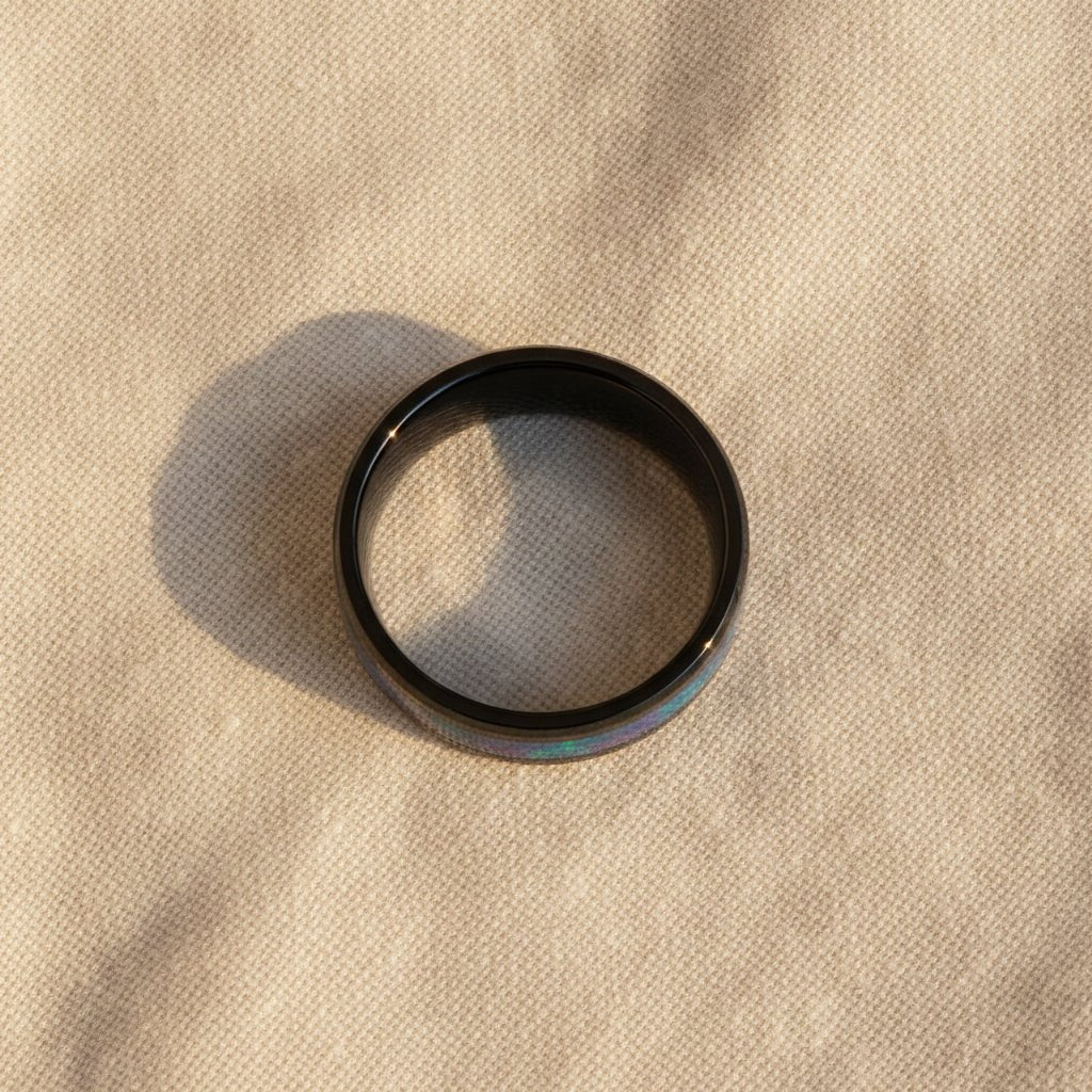 BARRACUDA black ceramic wedding band with blue and purple color-changing opal inlay running around the band and polished beveled edges macro detail overhead flat lay