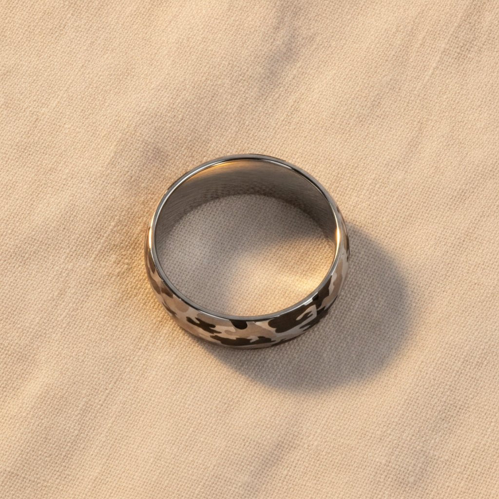 BATTALION domed silver tungsten carbide wedding band with laser engraved camouflage pattern running around the band and polished edges macro detail overhead flat lay
