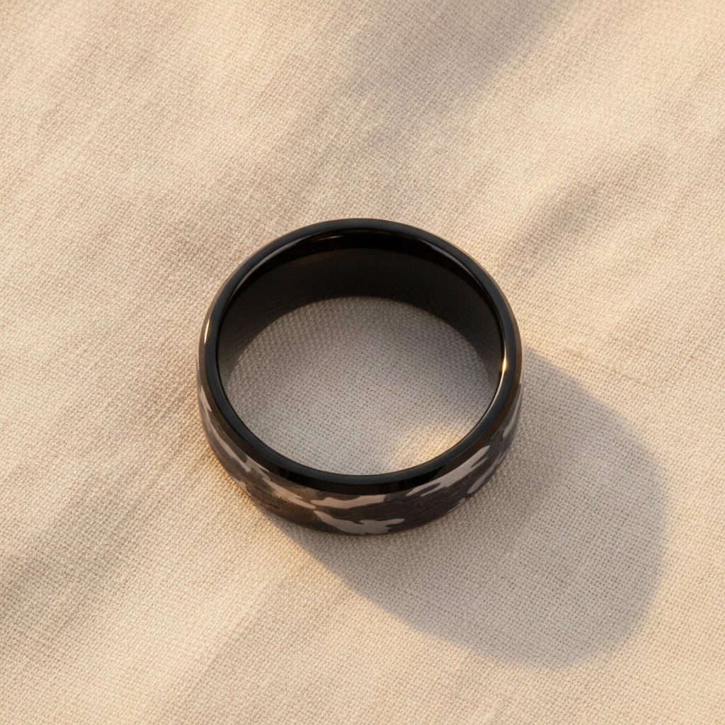 CONQUEST beveled black tungsten carbide wedding band with black and gray camouflage pattern inlay running around the band and polished edges macro detail overhead flat lay