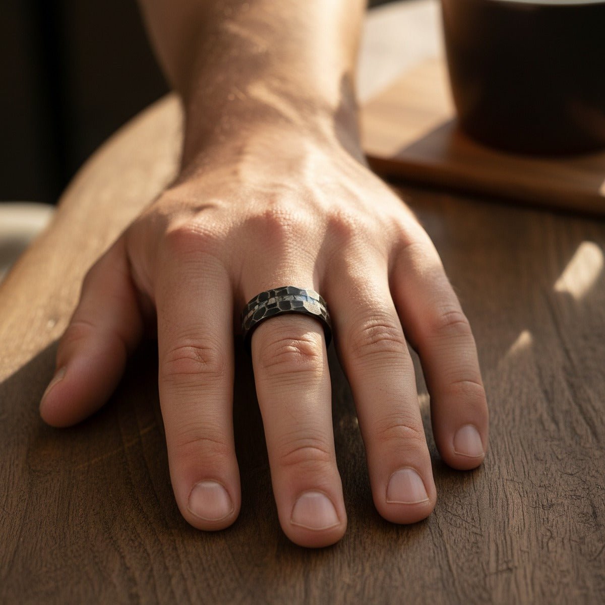 FISSURE black tungsten ring worn on a male hand resting on weathered wood, lifestyle scene