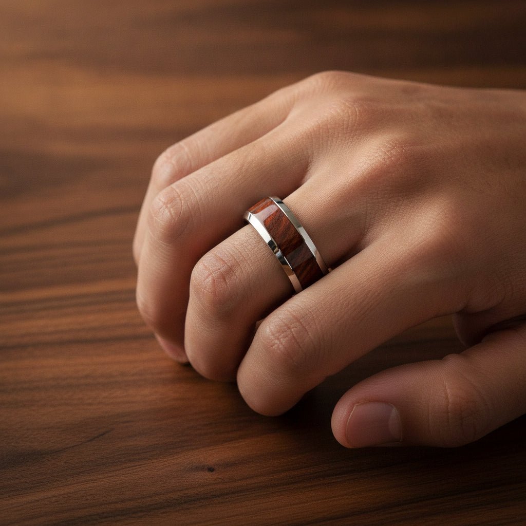 GROVE silver tungsten carbide wedding band with redwood inlay running around the band and polished edges worn on man's hand resting on walnut wood, lifestyle photo