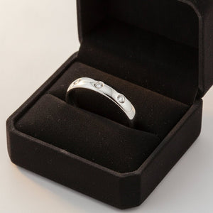 ISABELLA domed white tungsten wedding band with three small diamond accent stones set in a row on the center of the band and polished edges nested in a black velvet ring box, editorial jewelry shot