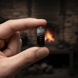 JUNCOS — Held between fingers close-up — men's tungsten wedding ring.