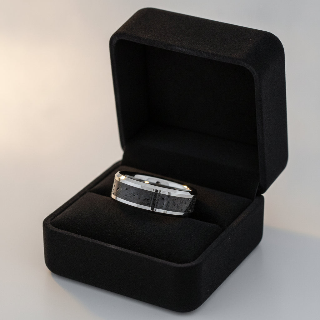 KILAUEA polished silver tungsten wedding band with black and gray lava rock stone inlay running around the band and polished beveled edges nested in a black velvet ring box, editorial jewelry shot