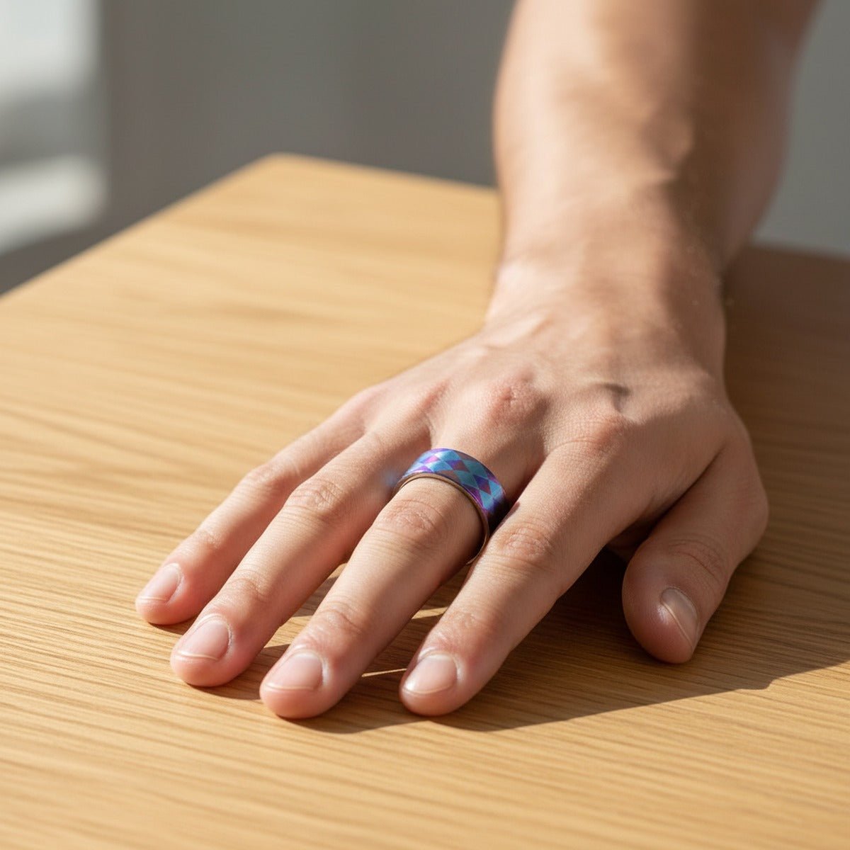 MERIDIAN flat titanium ring worn on a male hand resting on light wood, lifestyle scene