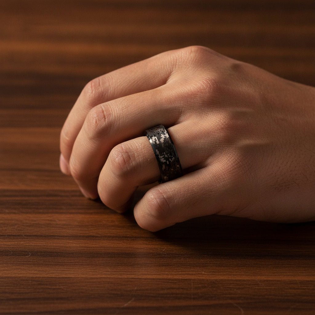 SMOKESCREEN black tungsten carbide wedding band with engraved digital camouflage pattern running around the band and polished edges worn on man's hand resting on walnut wood, lifestyle photo
