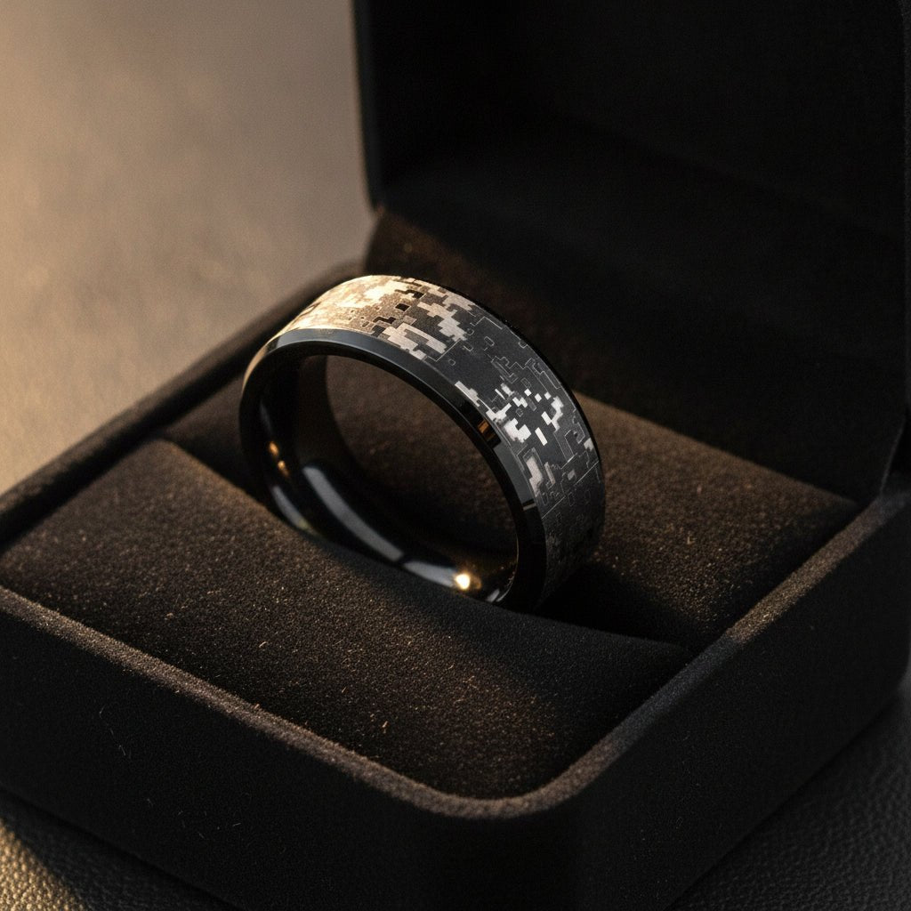 SMOKESCREEN black tungsten carbide wedding band with engraved digital camouflage pattern running around the band and polished edges nested in a black velvet ring box, editorial jewelry shot