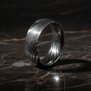 SWIRL — Luxury 3/4 angle on dark marble — men's tungsten wedding ring.