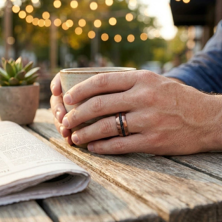 Aydins Jewelry Modern men’s tungsten wedding band with espresso finish and black sapphires on a mans ring finger holding a coffee cup