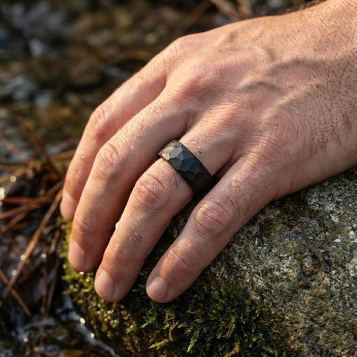 Aydins Jewelry Matte black tungsten hammered wedding band for men on a ring finger outdoors