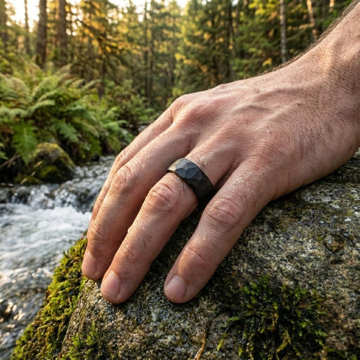 Aydins Jewelry Matte black tungsten hammered wedding band for men outdoors on a mans ring finger