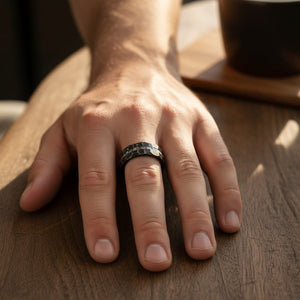 FISSURE black tungsten ring worn on a male hand resting on weathered wood, lifestyle scene