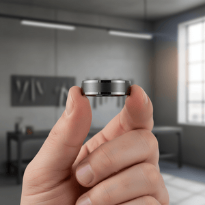 IGNITION — Held between fingers close-up — men's tungsten wedding ring.