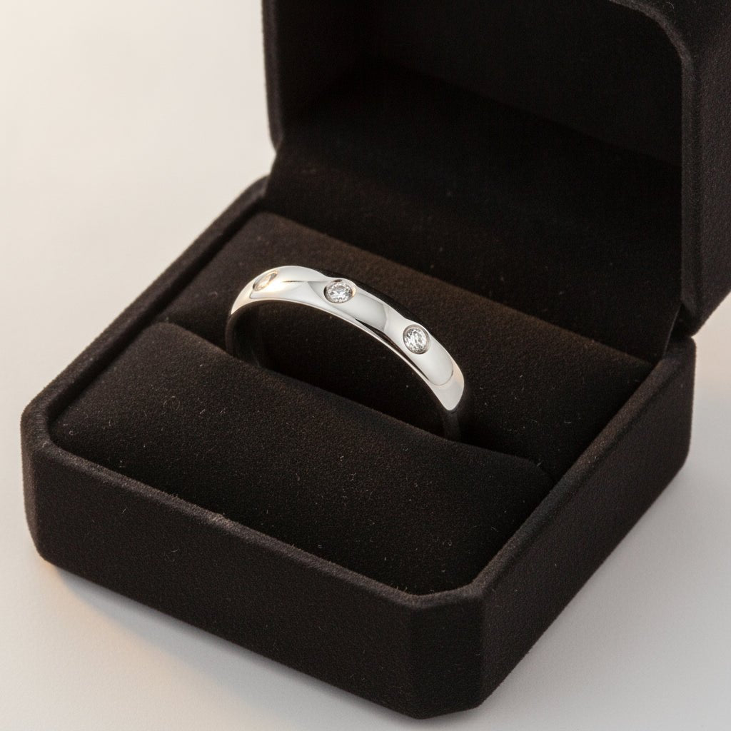 ISABELLA domed white tungsten wedding band with three small diamond accent stones set in a row on the center of the band and polished edges nested in a black velvet ring box, editorial jewelry shot