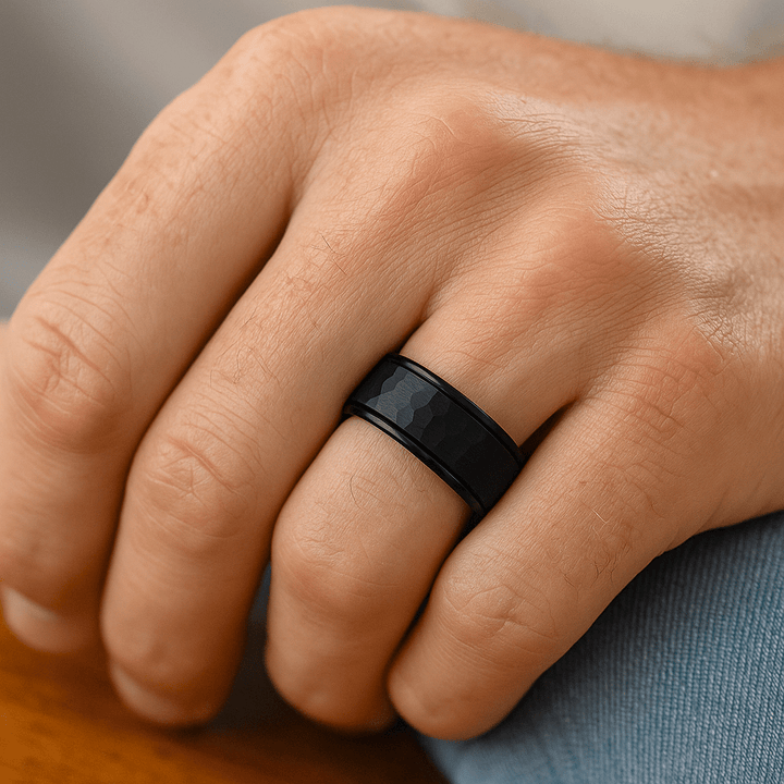 Close-up of a hand wearing a black ring on a neutral background