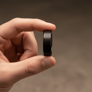 LOVELL — Held between fingers close-up — men's tungsten wedding ring.