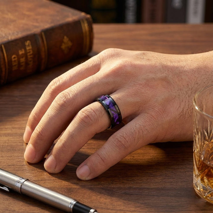 LUSTERS Black Tungsten Ring with Purple Tiger Cowrie Inlay on a ring finger near a whiskey glass