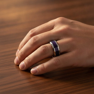 MAKI polished silver tungsten wedding band with sparkling purple goldstone inlay running around the band and polished beveled edges worn on man's hand resting on walnut wood, lifestyle photo