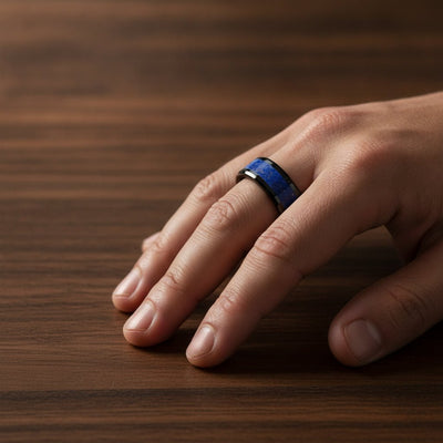 MARLOW polished black ceramic wedding band with blue lapis stone inlay running around the band and polished beveled edges worn on man's hand resting on walnut wood, lifestyle photo