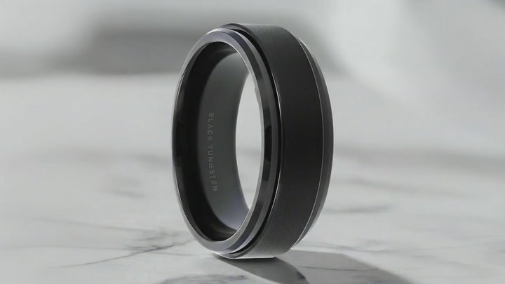 A black tungsten spinner fidget ring with beveled edges, displayed on a grey background video