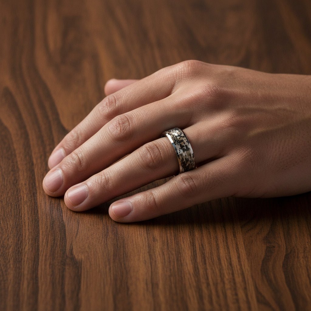 STEALTH silver tungsten carbide wedding band with engraved digital camouflage pattern running around the band and polished edges worn on man's hand resting on walnut wood, lifestyle photo