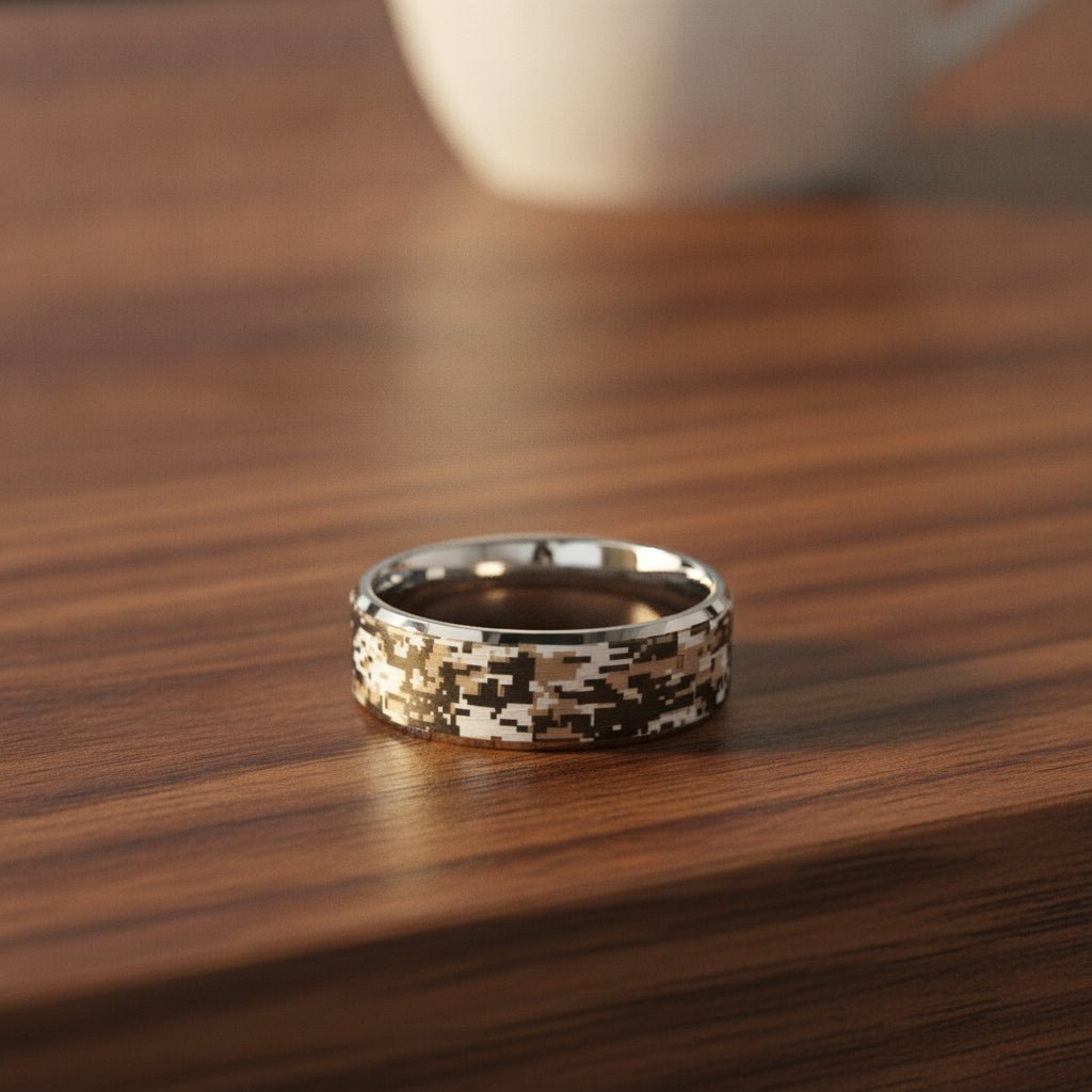 STEALTH silver tungsten carbide wedding band with engraved digital camouflage pattern running around the band and polished edges resting on a walnut wood counter, lifestyle scene