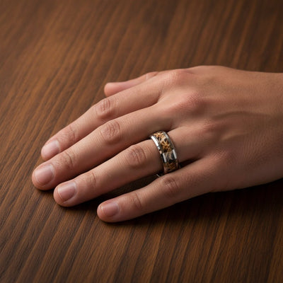 TERRA silver tungsten carbide wedding band with leaves and grassland woodland camouflage inlay running around the band and polished edges worn on man's hand resting on walnut wood, lifestyle photo