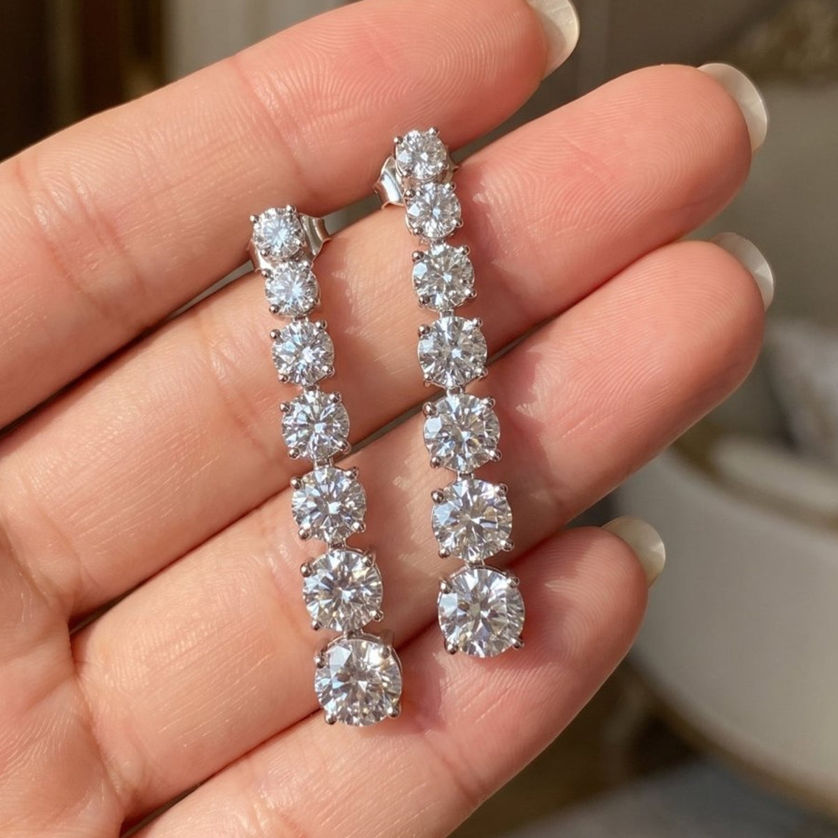 Graduated lab-grown diamond earrings in sterling silver, held in hand, close-up