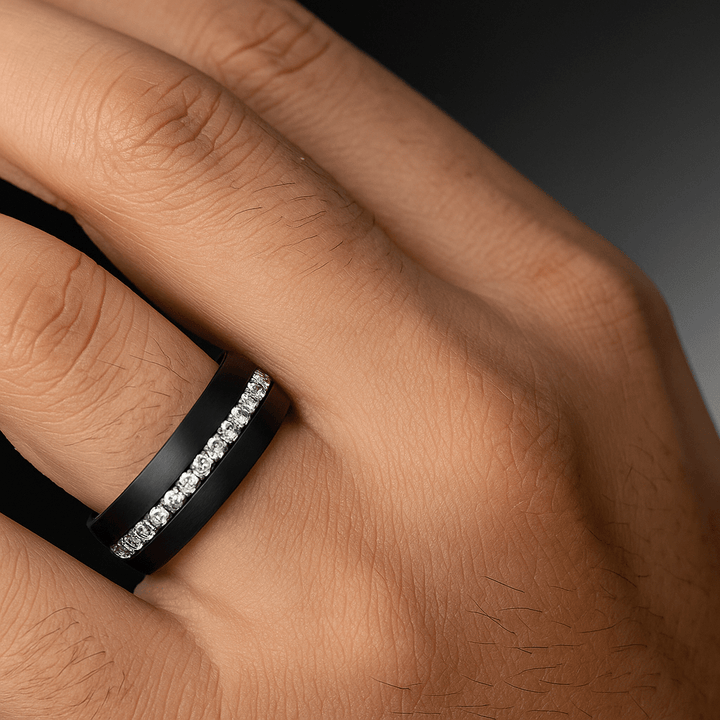 Close‑up of white sapphires set in brushed black tungsten band on a ring finger