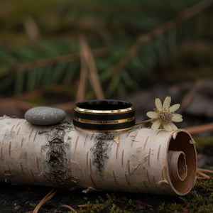 Aydins VERTEX | Polished Black Tungsten Yellow Gold Pinstripe Beveled Wedding Ring 8mm lifestyle scene, river birch bark